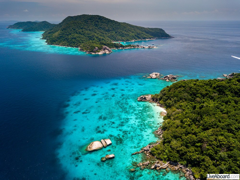 Aerial view of a deserted, jungle covered tropical island with crystal clear ocean below